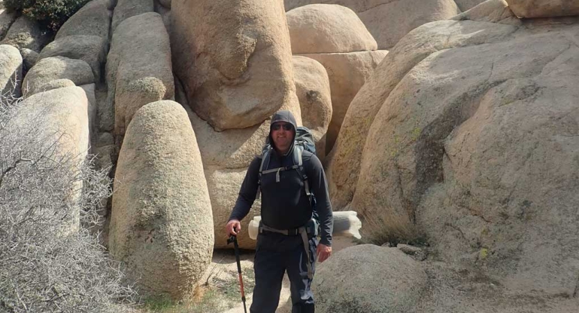 A person wearing hiking gear smiles for a photo while standing amid large boulders